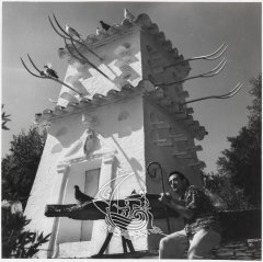 Fotografía de Salvador Dalí bajo la torre de la Casa Museo de Portlligat. La fotografía es en blanco y negro.