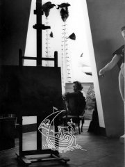 Black and white photograph. In the forefront of the image we can see a painting of Salvador Dalí in a room of his house in Portlligat. At the end of the image we can see the artist.