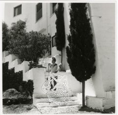 Salvador Dalí a les escales que pujaven a la casa de Portlligat. És una fotografia antiga en blanc i negre, on podem veure a l’artista amb una barretina al cap.