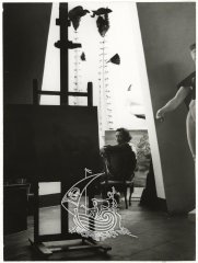 Vemos en primer plano una pintura de Dalí en el interior de la casa de Portlligat, y al fondo el artista de perfil, sentado en una silla.