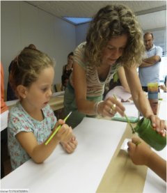 Una mujer enseña a una niña cómo hacer uso del pincel para pintar.