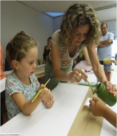 A woman teaches a little girl how to use a brush to paint.