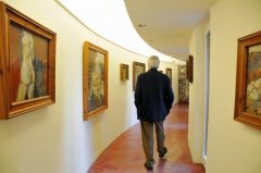 A man walks along a corridor of an exhibition of paintings of Antoni Pitxot i Soler.